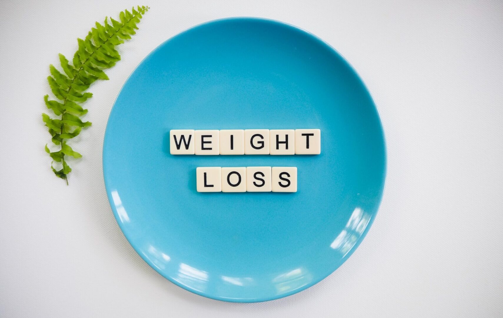A blue plate with the words weight loss spelled out in scrabble tiles.
