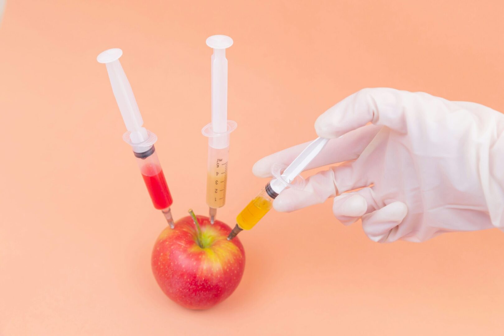 A hand holding three syringes in front of an apple.